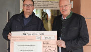 Kolping-Recycling-Geschäftsführer Stephan Kowoll (links) übergibt den 500,-€-Scheck an Bürgermeister Manfred Helfrich vor der Kindertagesstätte RhönKinder-Haus. (Foto: Gemeinde)