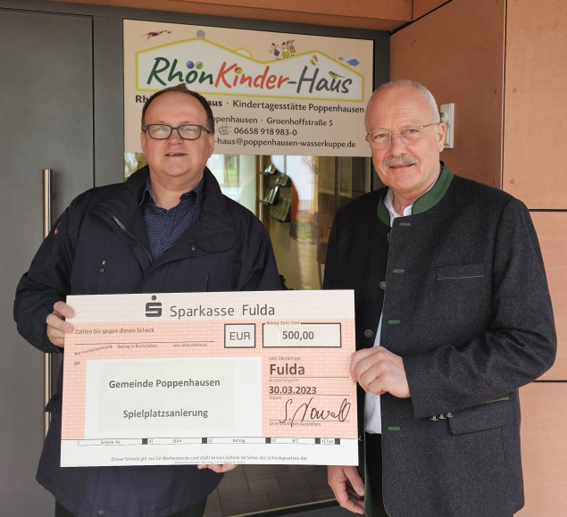 Kolping-Recycling-Geschäftsführer Stephan Kowoll (links) übergibt den 500,-€-Scheck an Bürgermeister Manfred Helfrich vor der Kindertagesstätte RhönKinder-Haus. (Foto: Gemeinde)